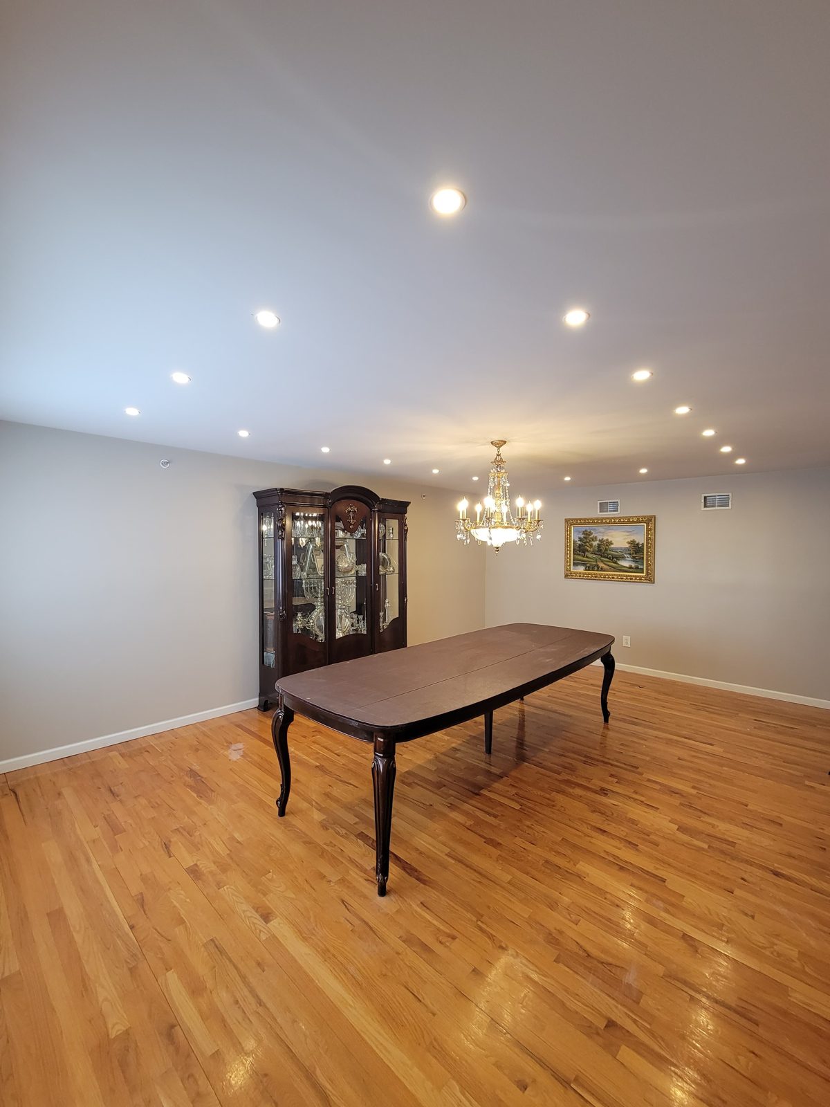 Dining table under a chandelier with recessed lighting on hardwood floors