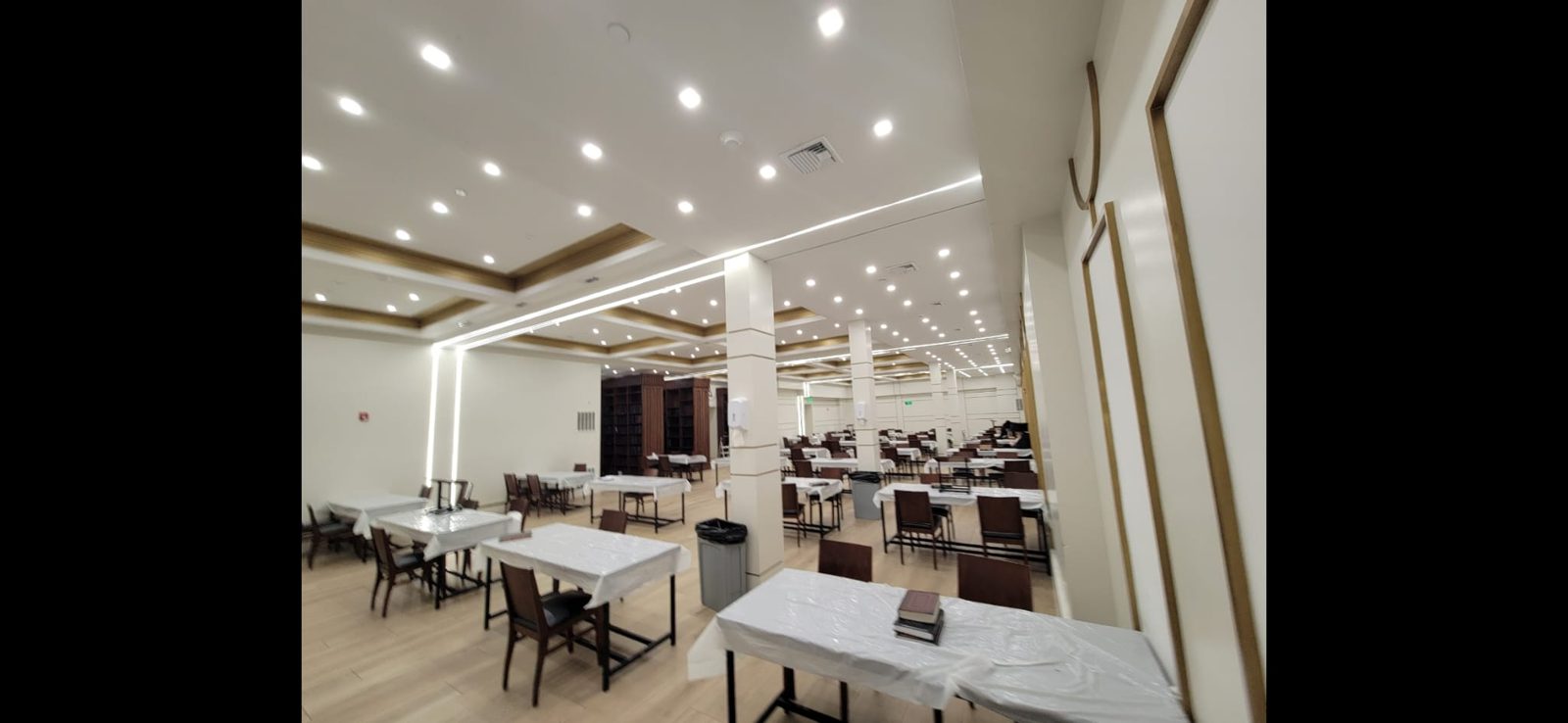 Large hall with linear LED cove lighting and rows of recessed downlights above dining tables