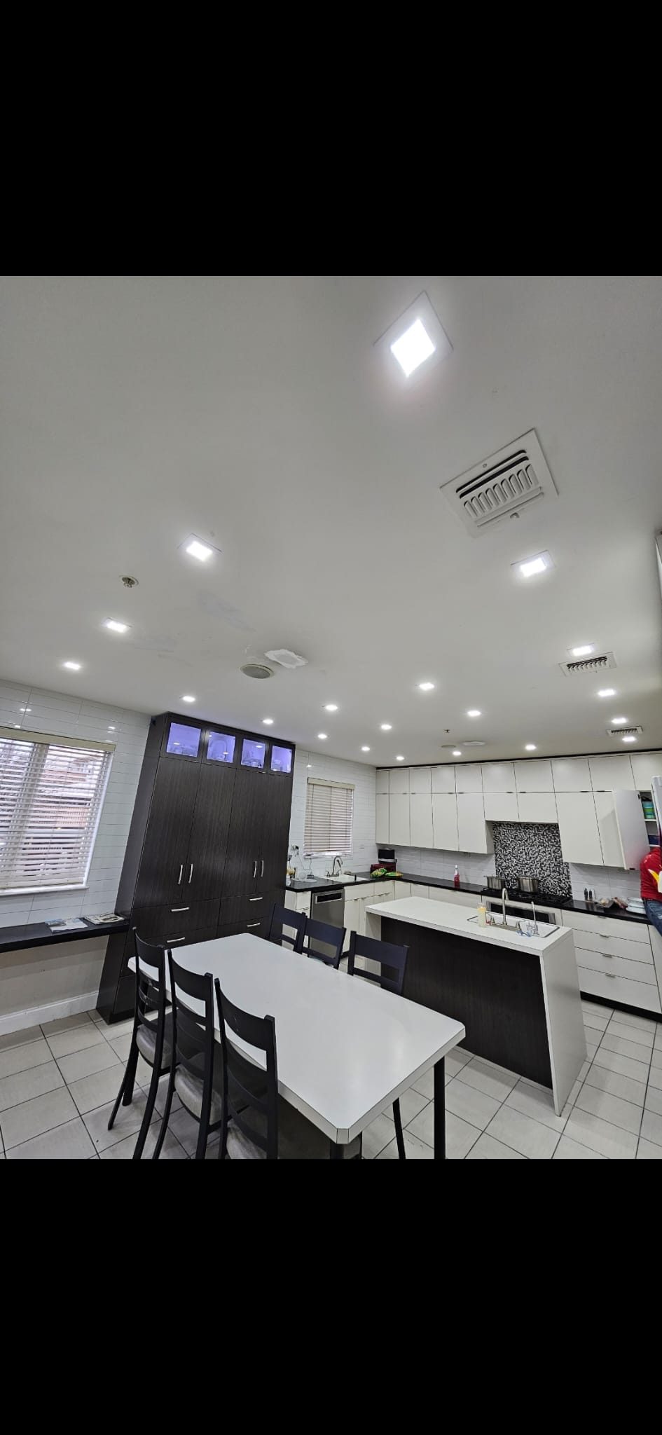 Kitchen with an island and dark cabinetry under bright recessed downlights
