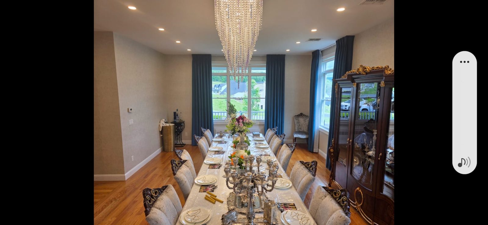 Long dining table beneath a large crystal chandelier with recessed perimeter lighting