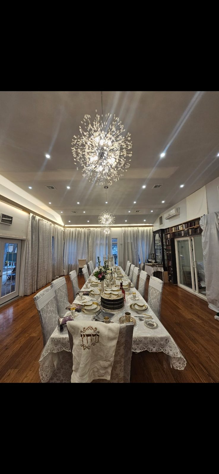 Crystal chandelier installed above a long set dining table with recessed lighting around it