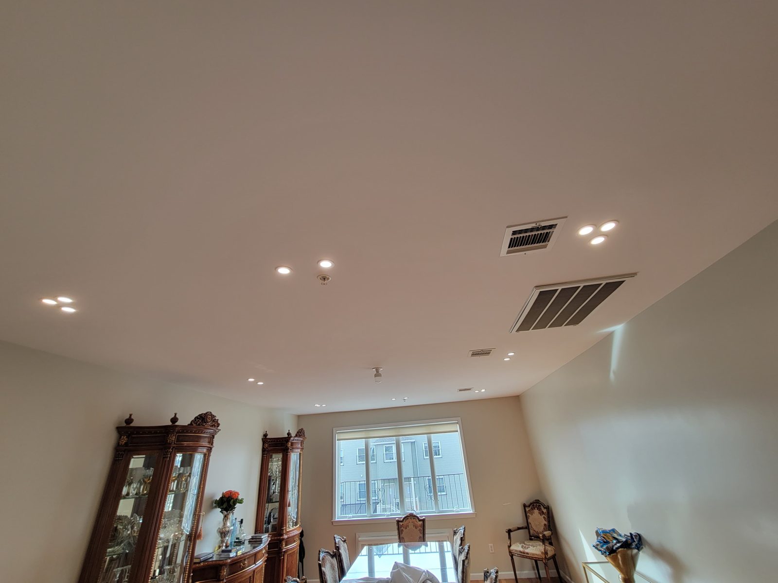Room with a display cabinet and window lit by recessed downlights